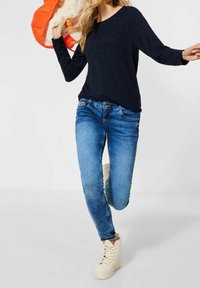 Haut à manches longues bleu marine, jean skinny bleu clair et baskets montantes crème. Le haut a un col rond ; le jean présente des poches classiques et des coutures.