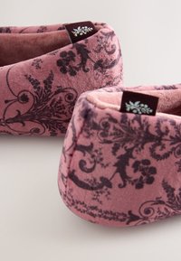 Pink plush slippers featuring dark floral patterns, rounded shape, soft texture, and small fabric tags at the back.