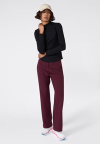 Top nero a maniche lunghe con una texture a coste, abbinato a pantaloni larghi bordeaux e sneakers bianche con dettagli rosa e blu. Cappellino beige.
