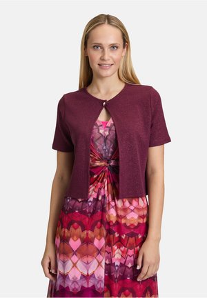 Bordeaux kort mouw cardigan met een ronde hals en een enkele knoopsluiting, gedragen over een kleurrijk gemusterde jurk met roze en oranje tinten.