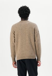 Maglione marrone lavorato a maglia con superficie testurizzata, collo girocollo e polsini e orlo a costine. Presenta leggere macchie su tutto il tessuto.