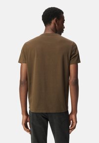 Camiseta de manga corta marrón con cuello redondo, hecha de una tela suave, que presenta un corte recto y mínimos detalles de costura en la parte posterior.