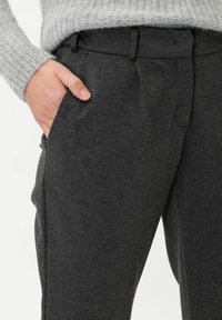 Tummanharmaat muotoonommellut housut, joissa on sileä pinta, sivutaskut ja litteä etuosa. Yhdistettynä vaaleanharmaaseen neulepaitaan.