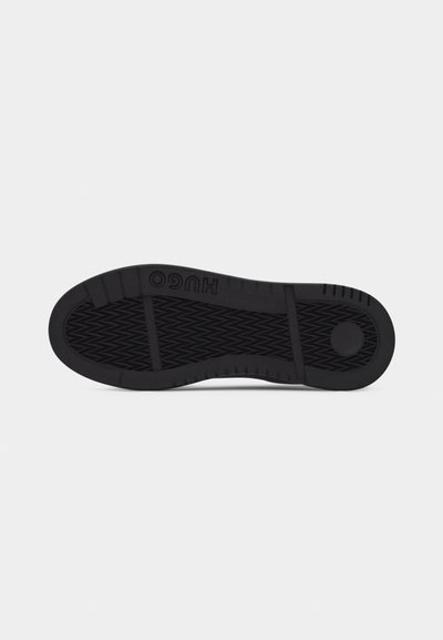 Semelle de chaussure en caoutchouc noir avec motif de bande de roulement texturé et nom de marque "HUGO" embossé près du talon sur un fond gris clair uni.