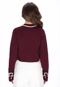 Suéter corto color burdeos con mangas largas, que presenta un borde decorativo blanco en el cuello y los puños, hecho de una tela suave.