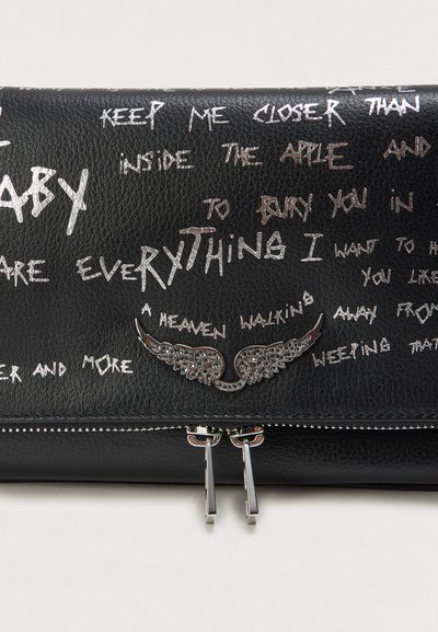 Musta nahkalompakko, jossa on hopeanvärinen siipeä muistuttava koristelu ja valkoista käsinkirjoitettua tekstiä hajallaan sen pinnalla.