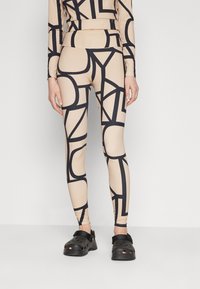 Beige leggings med svart abstrakt mønster, laget av stretchy stoff. Kombinert med svarte perforerte klippesko.