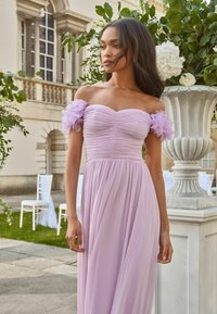 Rochie lila cu design off-shoulder, bust plisat și accente transparente, asemănătoare cu flori, pe manșete. Fustă fluidă, pliată, care se întinde până la sol.