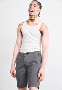 Shorts gris avec une ceinture élastique et un cordon de serrage, associés à un débardeur blanc ajusté. Tissu lisse avec un design simple.