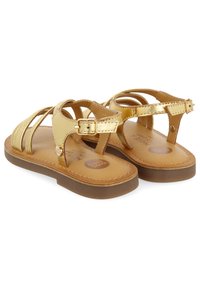Sandalias metálicas doradas con múltiples correas y cierre de hebilla. Suela texturizada marrón, plantilla acolchada y detalle circular del logotipo.