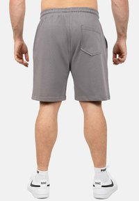 Grijze katoenen shorts met een elastische tailleband, zij- en achterzakken, en een rechte zoom. Gepaard met witte sneakers.