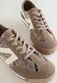 Braune Wildledersneaker mit einem Schlangenledermuster, strukturierten Akzenten und beigen Schnürsenkeln. Leichte Sohle mit geschwungenen Kanten und kontrastierenden weißen Details.