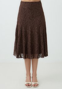 Brauner Spitzenrock mit einem ausgestellten Design, komplizierten Spitzenmustern und einem gewellten Saum. Das Tragen von weißen Sandalen mit offenen Zehen verbessert das Gesamtbild.