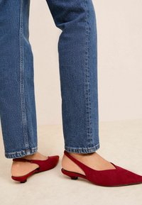 Pantofi slingback din suede roșu, cu vârf ascuțit și toc mic, asortați cu blugi drepți albaștri, evidențiind un look casual.