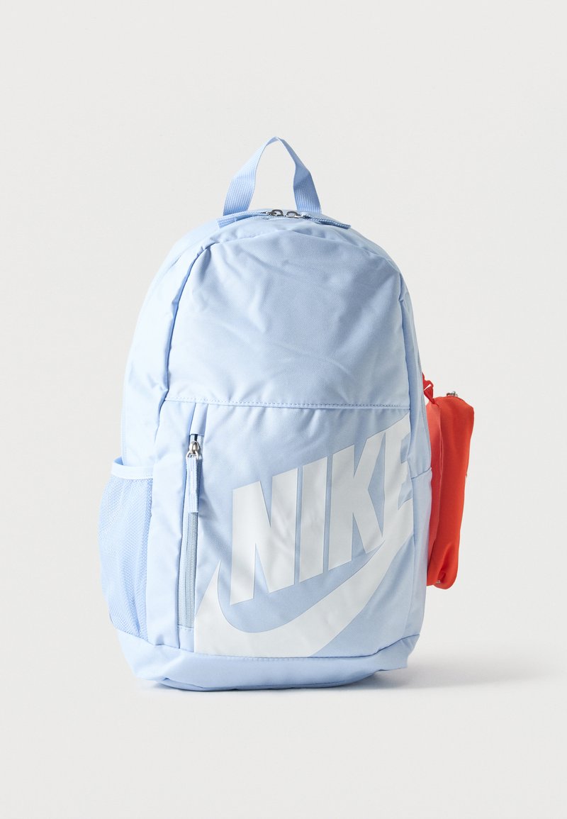 Ανοιχτό μπλε σακίδιο Nike με μεγάλο λευκό λογότυπο, μπροστινή τσέπη με φερμουάρ, πλαϊνή τσέπη με δίχτυ και προσαρτημένο μικρό κόκκινο τσαντάκι στη δεξιά πλευρά.