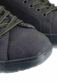 Sneaker in suede nero con finitura testurizzata, caratterizzate da lacci verdi e suole rotonde in gomma nera. La vista ravvicinata mette in evidenza il materiale e la forma.