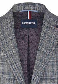 Blazer avec un motif écossais gris et une doublure marine, présentant une étiquette logo, un détail rayé contrastant et un col structuré.