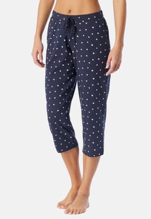 Pantalon de pyjama court bleu marine à pois blancs, taille élastique avec cordon, porté par une personne debout visible de la taille aux pieds.