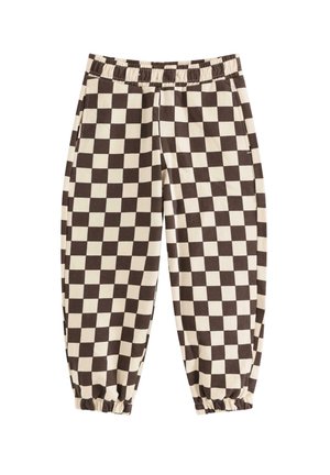 Barn iført en brun strikhue, farveblok-sweatshirt med flyvemaskine-patch, ternede bukser og brune snøresko, står og smiler.