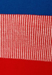 Tejido de punto con patrones texturizados en azul, rojo y rayas. La sección roja tiene rayas blancas alternando entre delgadas y gruesas.