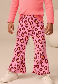Leggings roses évasés avec un motif léopard dans des tons foncés et clairs, dotés d'une texture côtelée et d'un détail d'ourlet ondulé.
