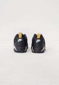Melni Nike sporta apavi ar zelta akcentiem, ar struktūrizētu aizmuguri, nostiprinātu papēdi un kontrastējošu baltu logotipu. Ir vilkšanas cilpa vieglai uzvilkšanai.