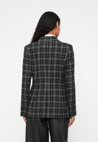 Sako na kariricu u crno-bijeloj boji s krojem po mjeri, sa zaklopnim ovratnikom i detaljima na gumbima, u kombinaciji s crnim širokim hlačama.