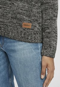 Grå och svart stickad tröja med ribbat avslut och en läderetikett med texten "OXMO". Matchad med ljusblå denimjeans.