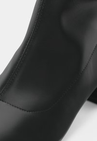 Μαύρο δερμάτινο μποτάκι μέχρι τον αστράγαλο με λείο φινίρισμα, με κομψό σχέδιο και ορατές ραφές στο πλάι για επιπλέον λεπτομέρεια.