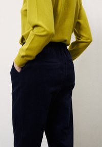 Pantalons en velours côtelé bleu marine à coupe décontractée, avec un motif texturé en stries et une taille élastique, associés à un haut vert à manches longues.
