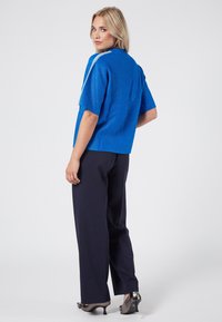 Maglietta blu a maniche corte con finitura texture e leggere righe sulle spalle, abbinata a pantaloni a gamba larga scuri e tacchi lucidi.