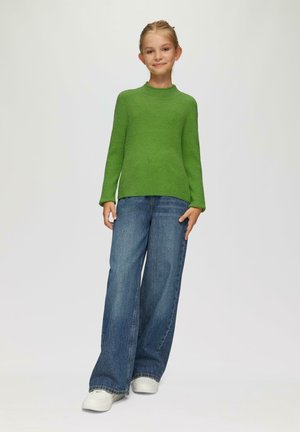 Grüner gerippter Strickpullover mit langen Ärmeln, kombiniert mit dunkelblauben weit geschnittenen Jeans und weißen Sneakers. Einfacher, lässiger Stil.