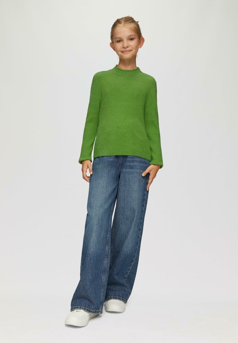 Grüner gerippter Strickpullover mit langen Ärmeln, kombiniert mit dunkelblauben weit geschnittenen Jeans und weißen Sneakers. Einfacher, lässiger Stil.