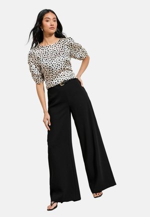 Schwarze Hosen mit weitem Bein, kombiniert mit einem cremefarbenen Kurzarmshirt mit schwarzem Polka-Dot-Muster und tailliertem Gürtel. Glatte Textur.