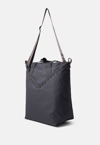 Sac fourre-tout en tissu noir avec un bord festonné ; dispose de deux poignées et d'une longue bandoulière ajustable pour le port. Texture lisse.