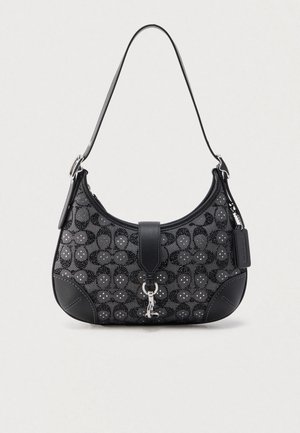 Musta käsilaukku, jossa on kuvioitu kangas pyöreillä kuvioilla, nahkaiset yksityiskohdat, litteä olkahihna ja metallinen lukko.