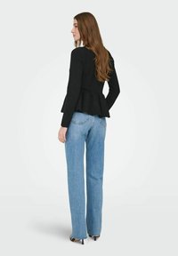 Peplum sort sweater med lange ærmer, tekstureret stof, kombineret med lyseblå jeans med lige ben og sko med hæl. Set bagfra.