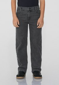 Černé džíny z denimu se střihovým provedením s rovnými nohavicemi, pěti kapsami a kontrastním šitím. V kombinaci s černými sportovními botami.