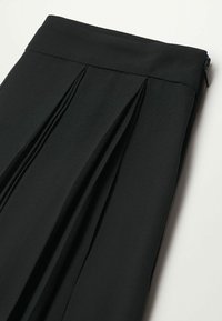 Falda plisada negra hecha de un tejido ligero, con una textura suave y un zipper lateral invisible. Diseño limpio y entallado.