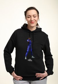 Sudadera negra con un gráfico vibrante en púrpura de un personaje en posición de combate. Capucha con cordones y textura suave.