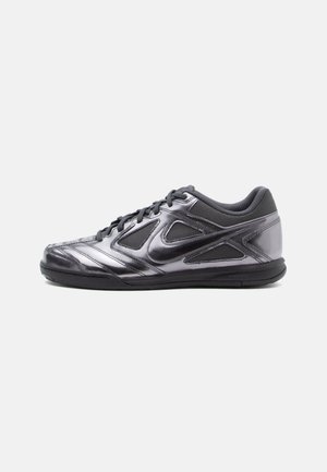 Black and metallic gray athletic shoe with mesh panels, smooth synthetic upper, textured sole, and lace-up design. Features a logo accent.