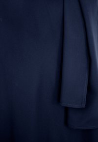 Granatowy materiał o gładkiej strukturze, z zagiętą sekcją po prawej stronie. Brak widocznych wzorów lub elementów metalowych.