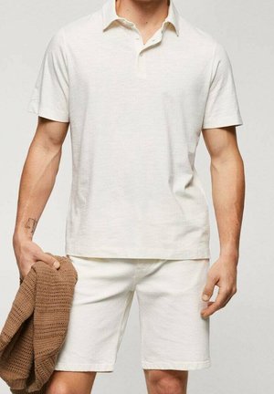 Hvid herre polo skjorte med krave, korte ærmer og løst fit, parret med hvide shorts. Han holder en struktureret brun sweater.