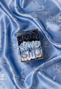 Set aus drei großen reinen Seidenscrunchies in Marineblau, Hellblau und Creme, präsentiert in einer Schachtel auf einem weichen blauen Satin-Hintergrund mit Schleifenmuster.