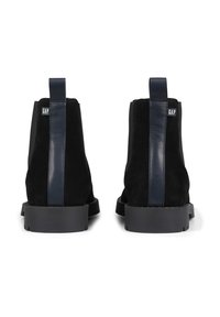 Botines de ante negro con un panel de cuero azul marino y tira en el talón. Presentan una suela de goma con ranuras de tracción y una etiqueta de marca.