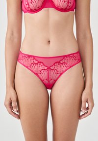 Slip rosa in lingerie con un corpo in rete trasparente e dettagli in pizzo floreale lungo l'elastico in vita, caratterizzato da bordi scallop e motivi intricati.