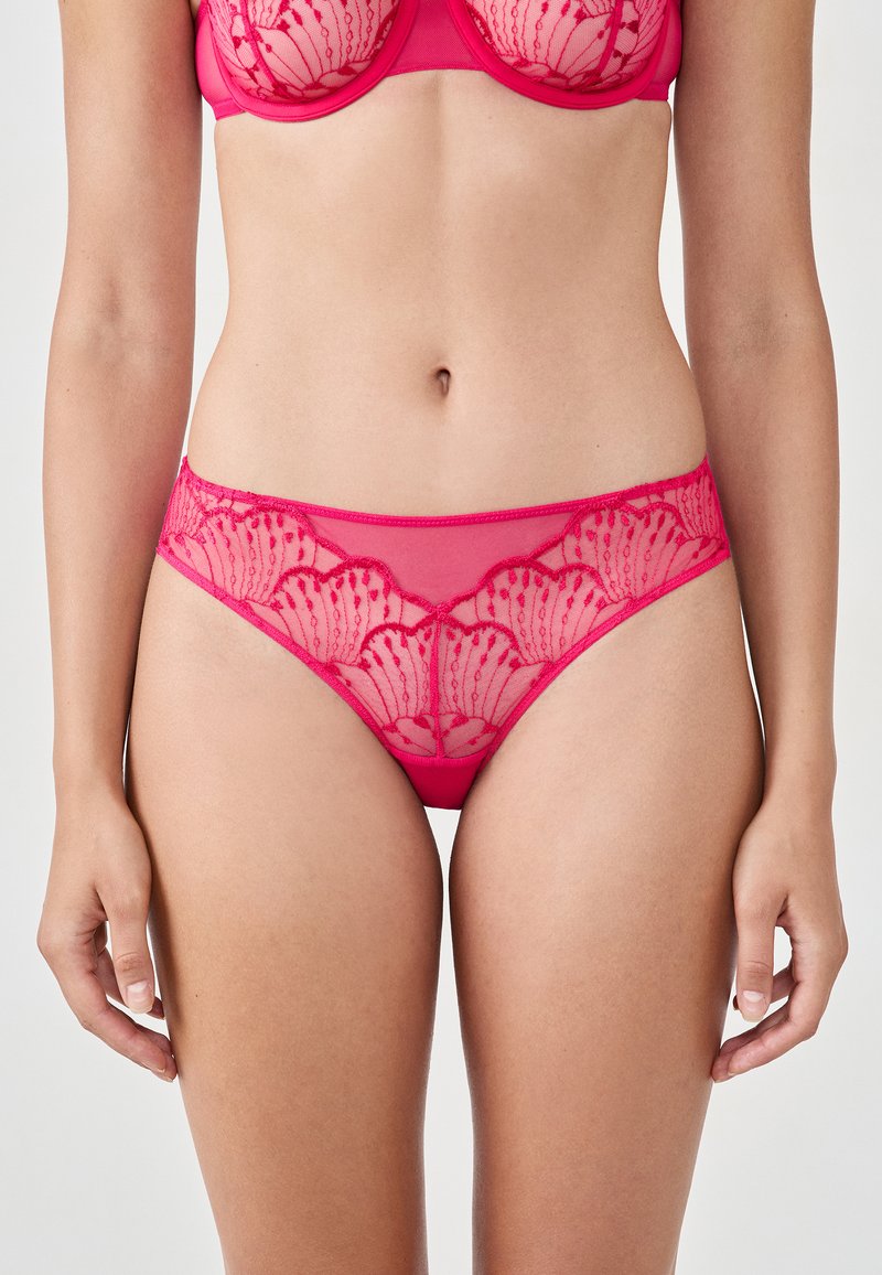 Slip rosa in lingerie con un corpo in rete trasparente e dettagli in pizzo floreale lungo l'elastico in vita, caratterizzato da bordi scallop e motivi intricati.