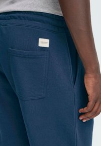 Pantalones de chándal en color navy que presentan una tela suave, cintura elástica, bolsillo lateral y una pequeña etiqueta con "GBLEND" en la parte posterior.