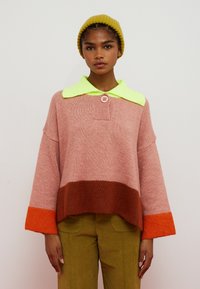 Colorblocket sweater i pink, brun og orange med en neongrøn krave, knappedetalje og brede ærmer. Blød strikket tekstur.