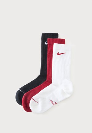 Τρεις κάλτσες Nike crew σε μαύρο, κόκκινο και λευκό με το λογότυπο Nike swoosh κοντά στο πάνω μανίκι σε ανοιχτό φόντο.